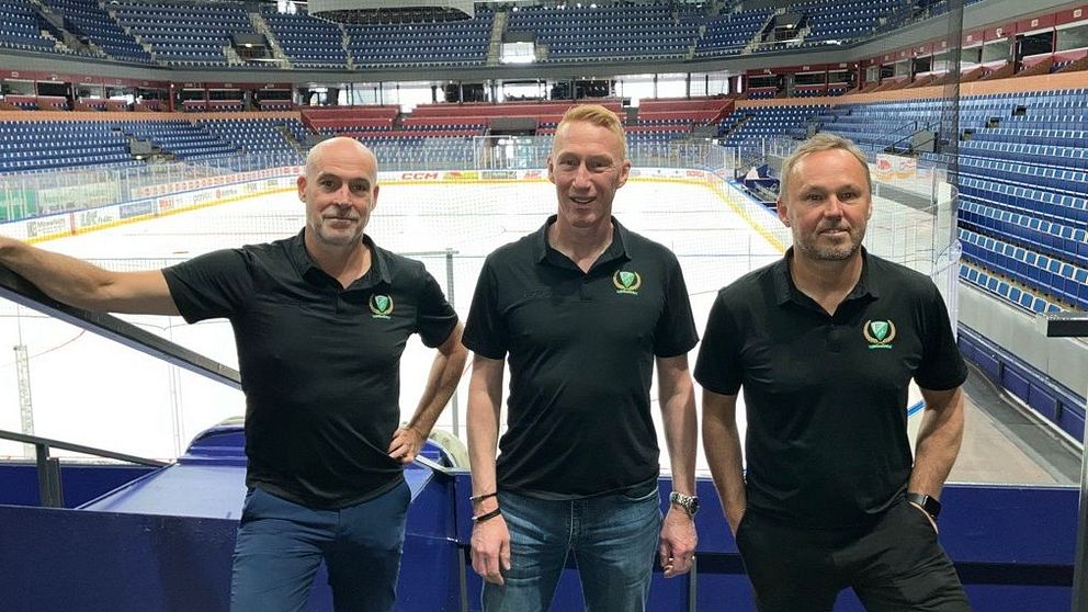 Tre personer i svarta pikétröjor står vid läktaren i en tom ishockeyarena.