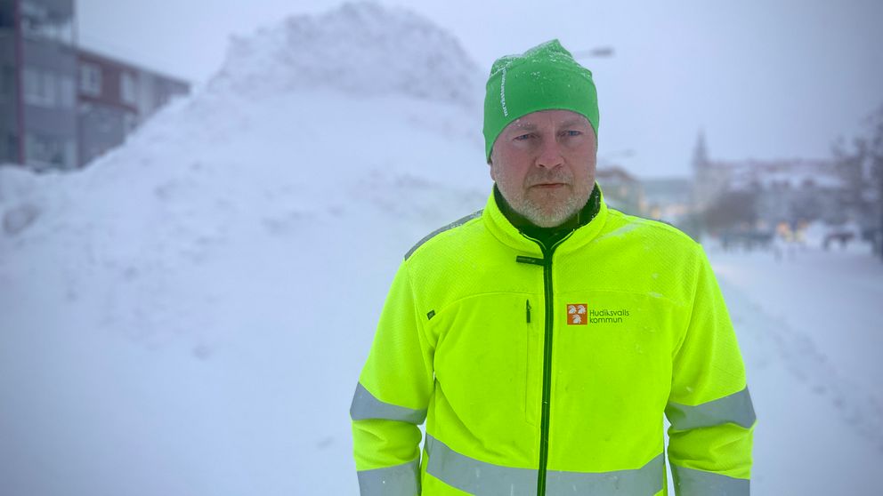 Gatuchef Peter Söderlund står iklädd Hudiksvall kommuns neonfärgade jacka. Bakom honom syns en ansenlig hög med snö.