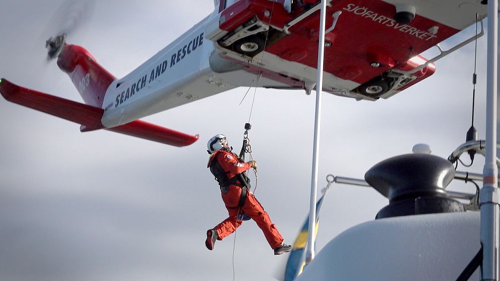 en ytbärgare hänger i vajer nedanför sjöräddningshelikopter.