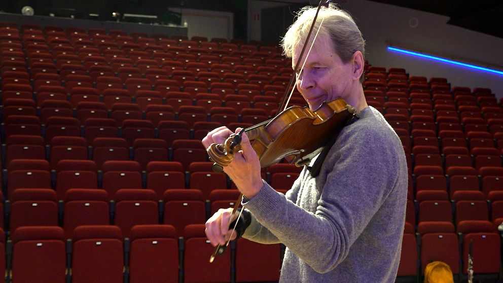 En man står i konserthall och spelar fiol.