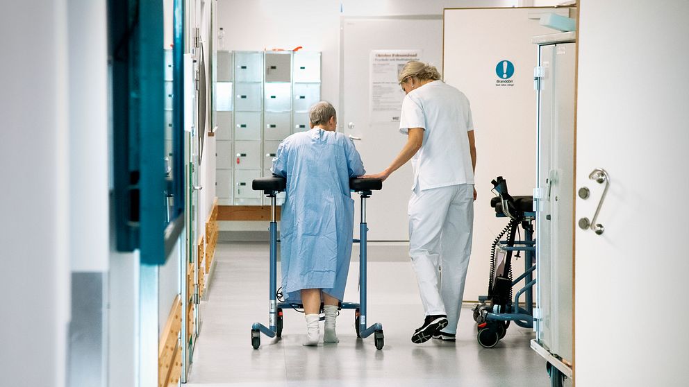 Sjuksköterska med patient i korridor på sjukhus.