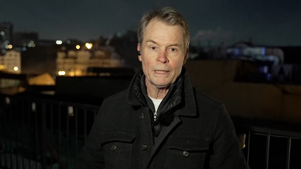 En person står på en balkong med utsikt över en stad belyst av gatlyktor en mörk natt.