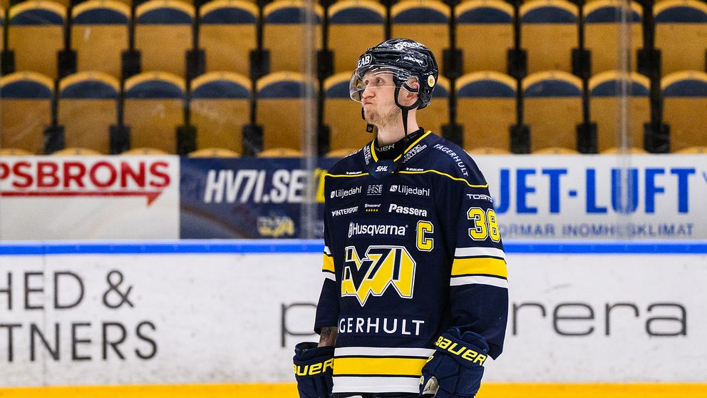 Ishockeyspelare från HV71 med hjälm och nummer 38 på tröjan står på isbanan.