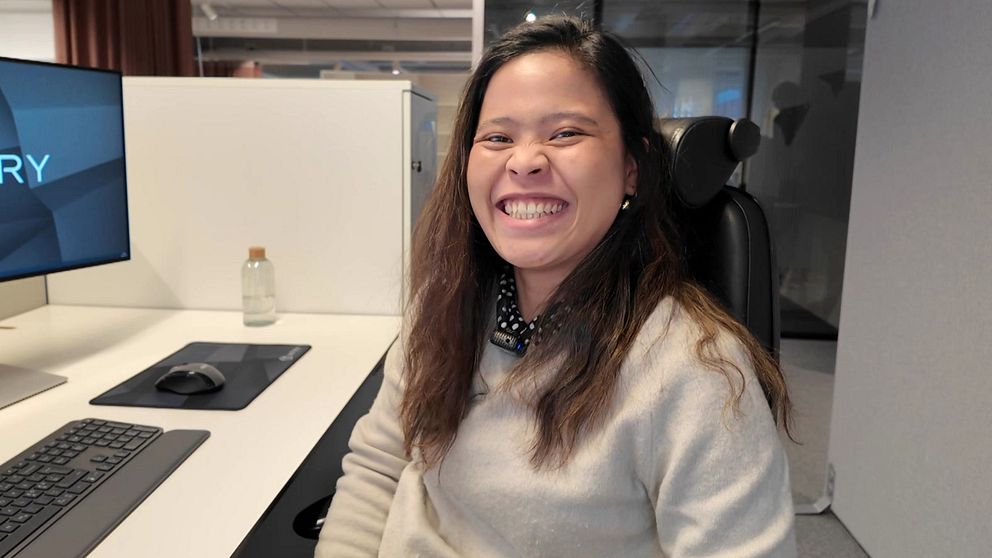 En ung kvinna sitter vid ett skrivbord på ett kontor och ser glad ut, efter att ha blivit anställd på ett nytt företag efter att hon tappade jobbet på Norhvolt.