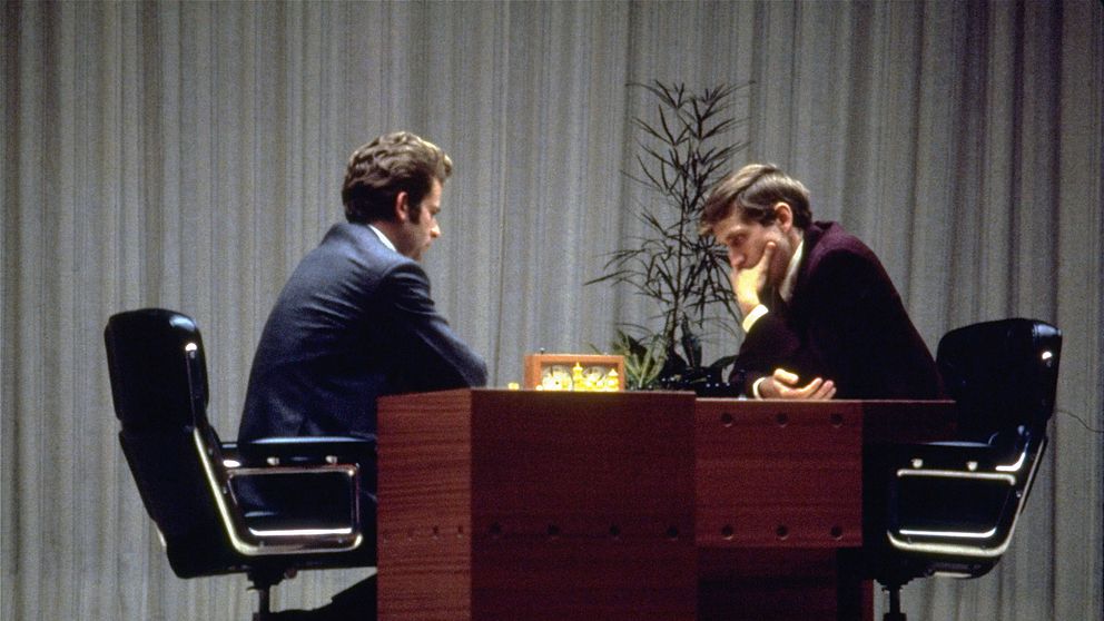Två män spelar schack vid ett bord, djupt koncentrerade.