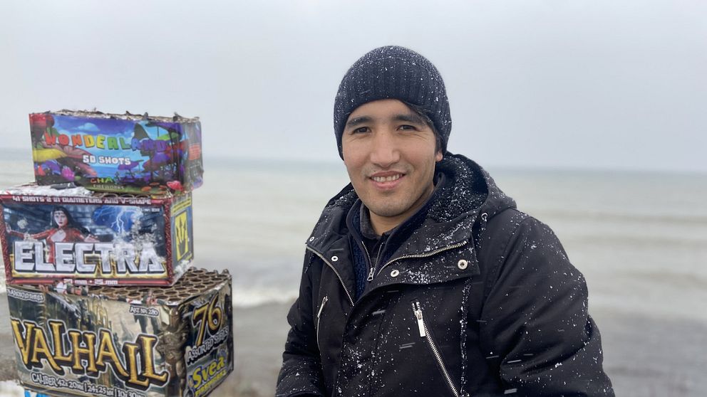 Amir Faqiri står utomhus bredvid ett torn av tomma fyrverkerikartonger.
