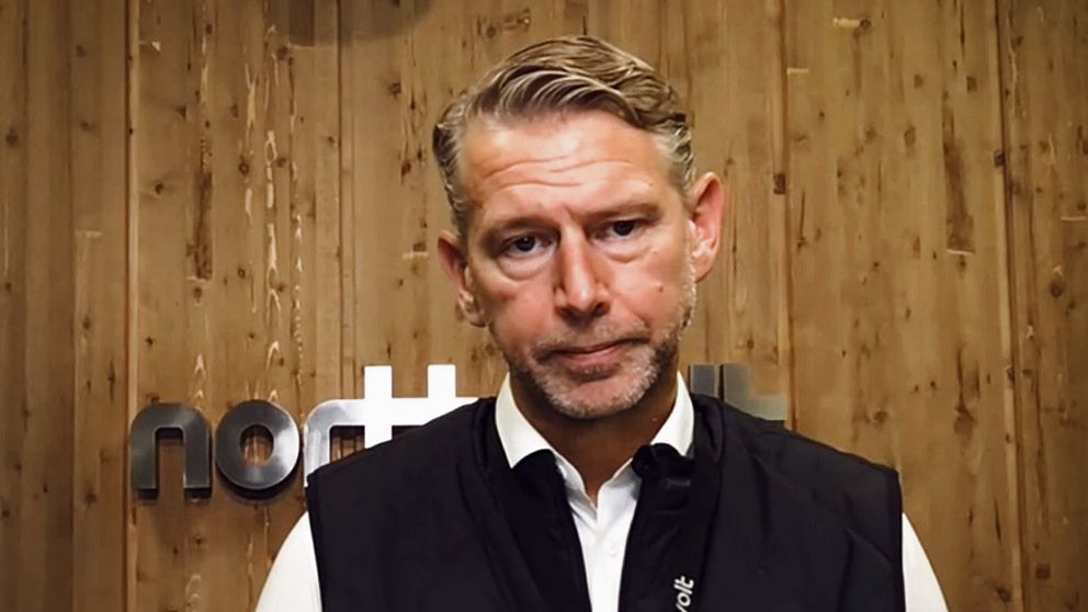 En person står framför en träpanel som har en logotyp för ”nothnet”. Personen bär en svart väst över en vit skjorta. Bakgrunden är mörk och varm, vilket skapar en professionell atmosfär.