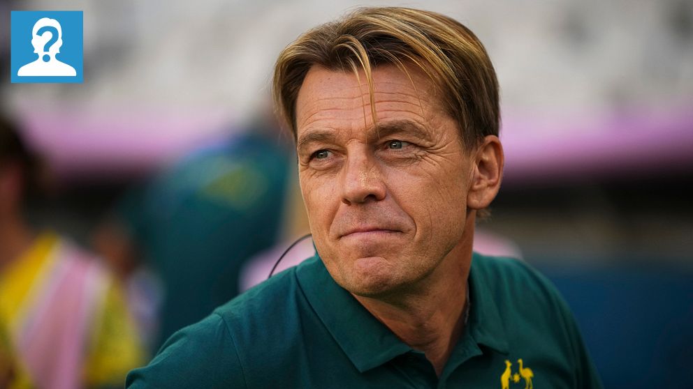 En person iklädd en grön tröja med Australiens olympiska logotyp står utomhus. I bakgrunden syns en suddig grupp av människor, varav en i en tröja med guldfärgade inslag.