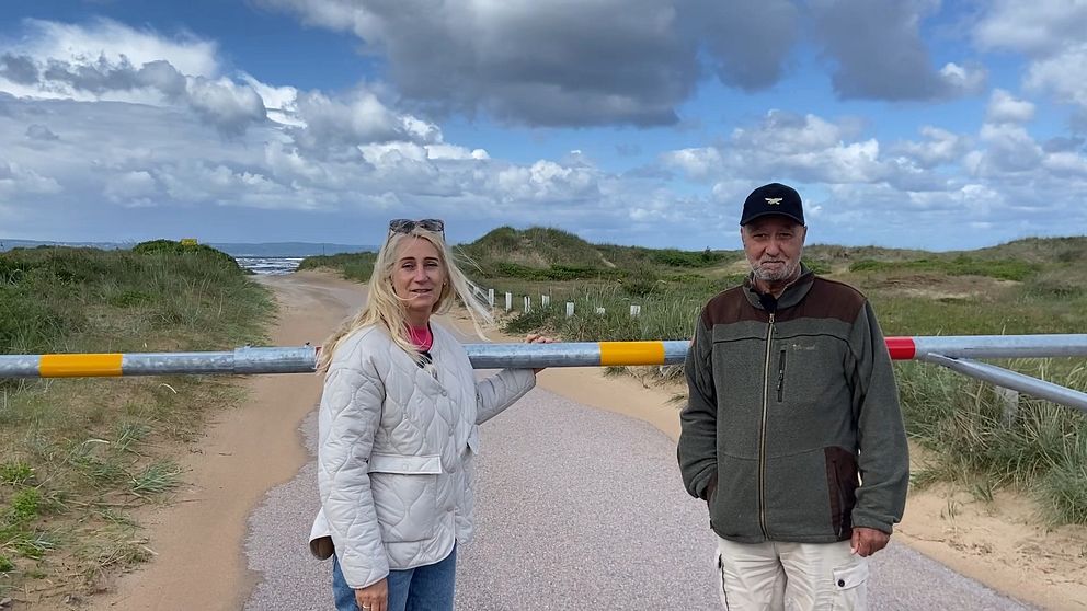 Chatarina Friiberg och Bengt Sjöberg står framför bommen de har tvingats sätta upp mot sin vilja vid den före detta bilstranden i Mellbystrand.