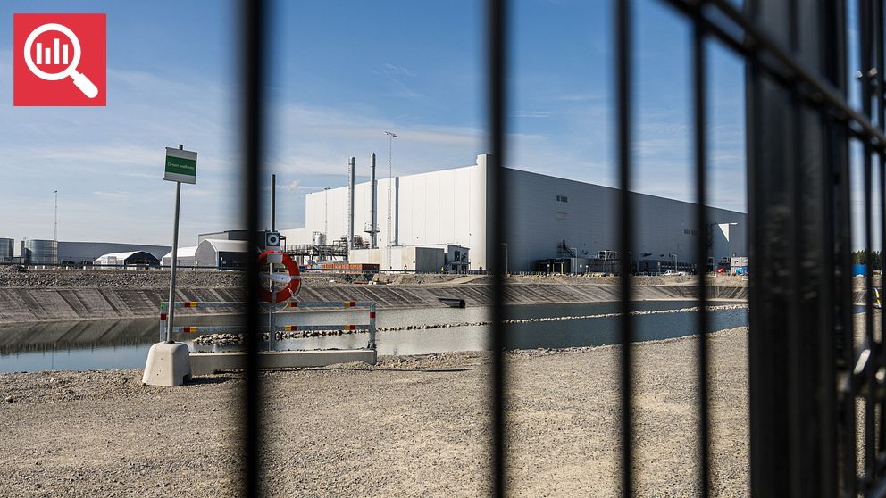 Industrianläggning bakom stängsel med vattenkanal i förgrunden.
