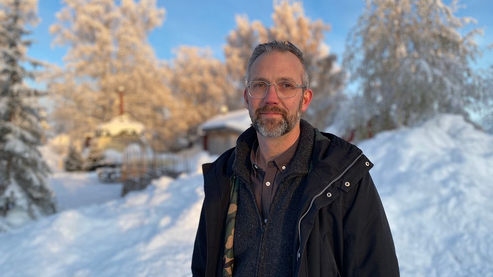Man med kort gråsprängt hår, gråsprängt skägg och glasögon står ute i ett vinterlandskap.