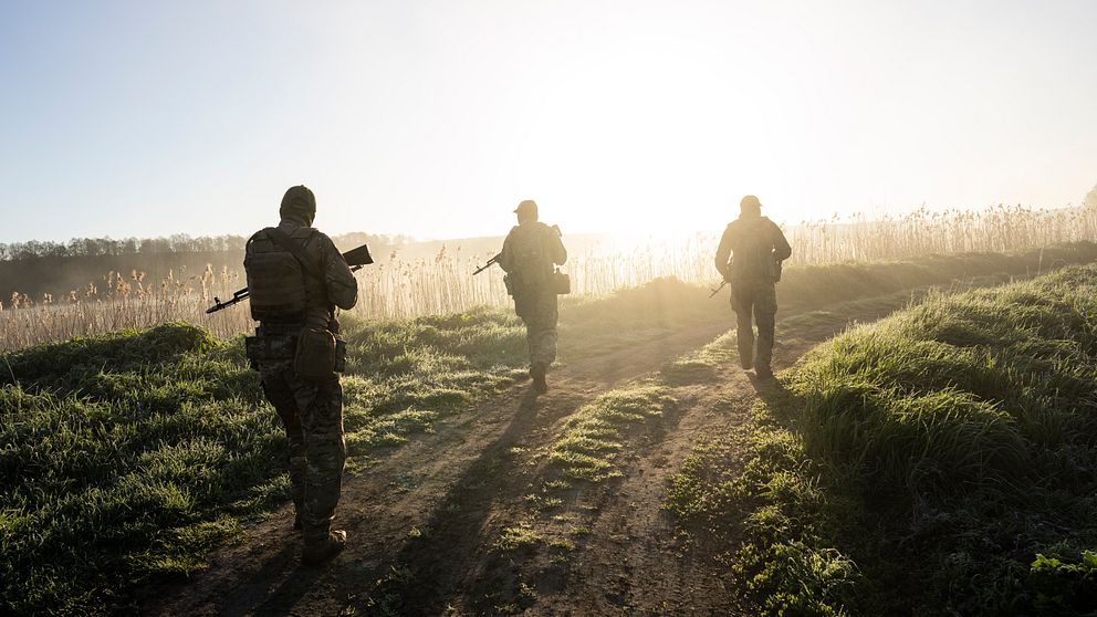 Tre soldater går på en väg i ett öppet landskap.