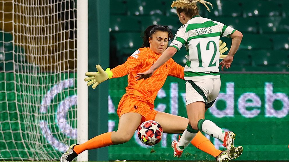 En fotbollsspelare i grönvitrandigt skjuter mot mål förbi målvakt i orange matchställ.