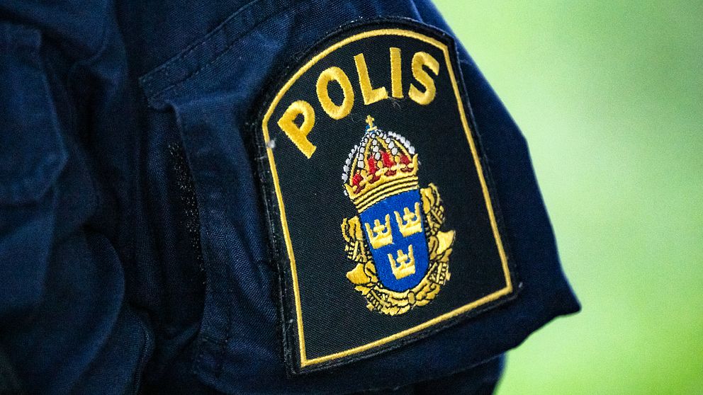 Närbild på svensk polisuniform med polisens emblem på ärmen.