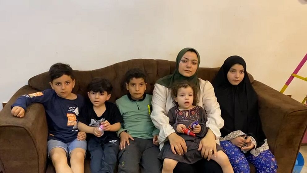 Mamma med fem barn sitter i en brun soffa