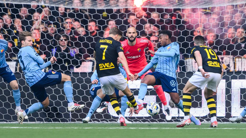 AIK och Djurgården-spelare slåss om bollen framför mål, publik med bengaler i bakgrunden.