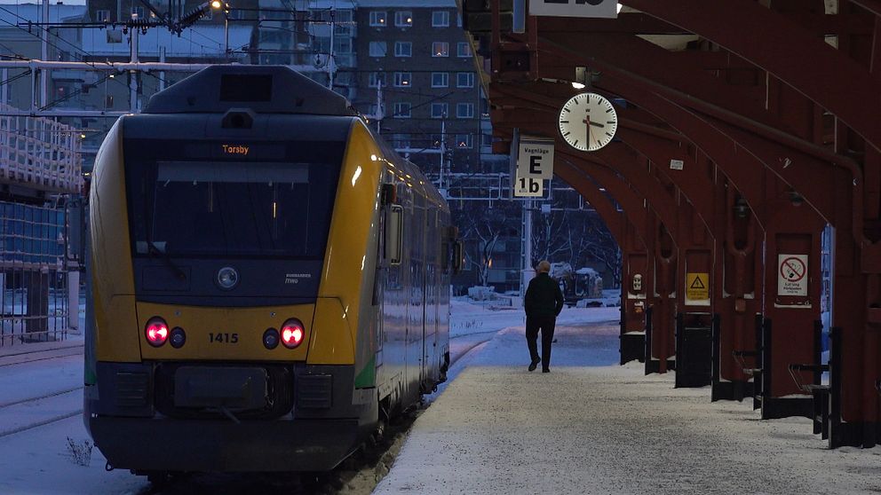 Ett tåg står vid en snötäckt perrong. Konduktören går på perrongen bredvid tåget