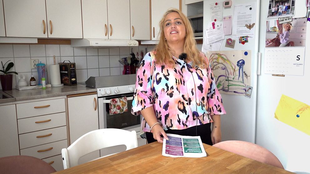 Madelene Eddaoui står vid sitt köksbord med en folder i handen.