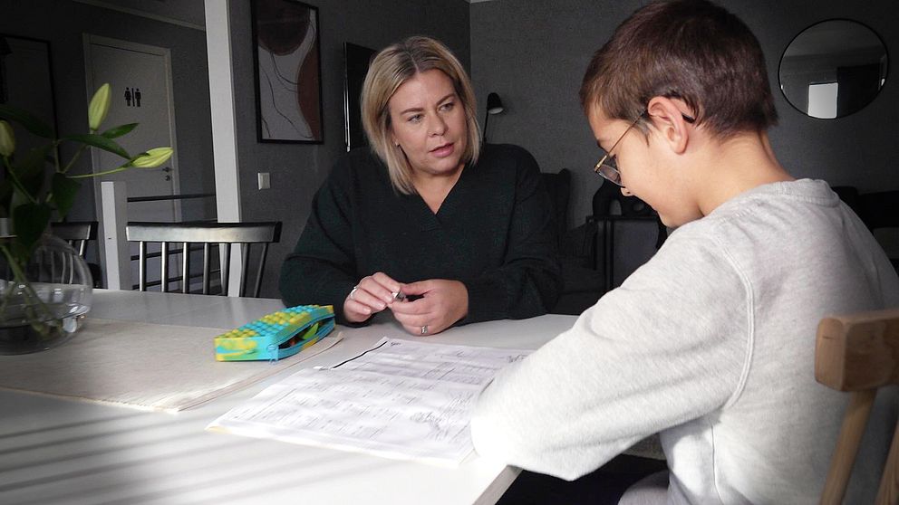 En pojke och en kvinna sitter vid ett matbord och gör matteläxa