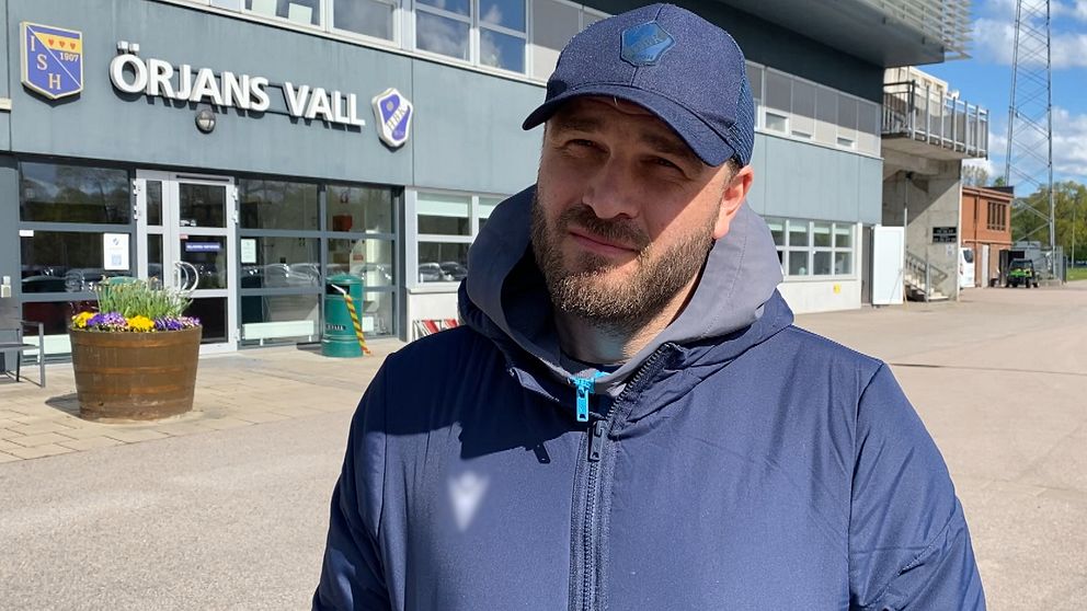 Person i blå jacka står framför Örjans Vall-stadions entré i solsken.