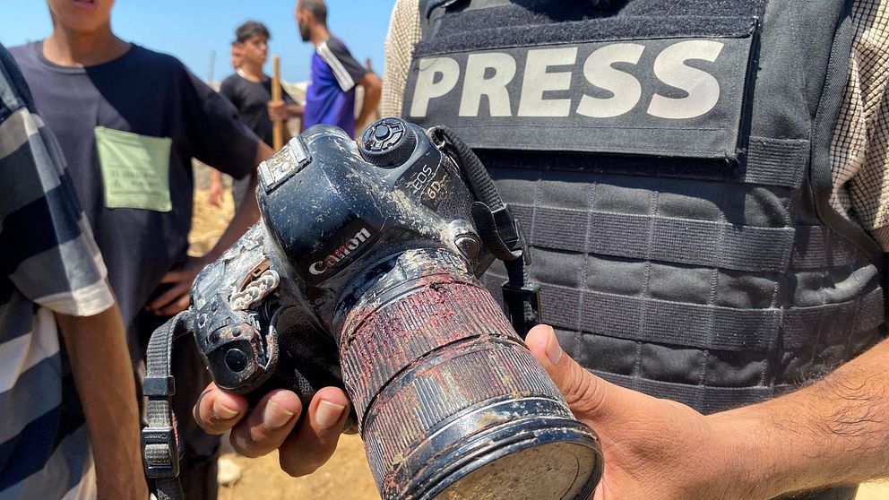 Journalist visar upp en skadad kamera med brända och smutsiga delar.