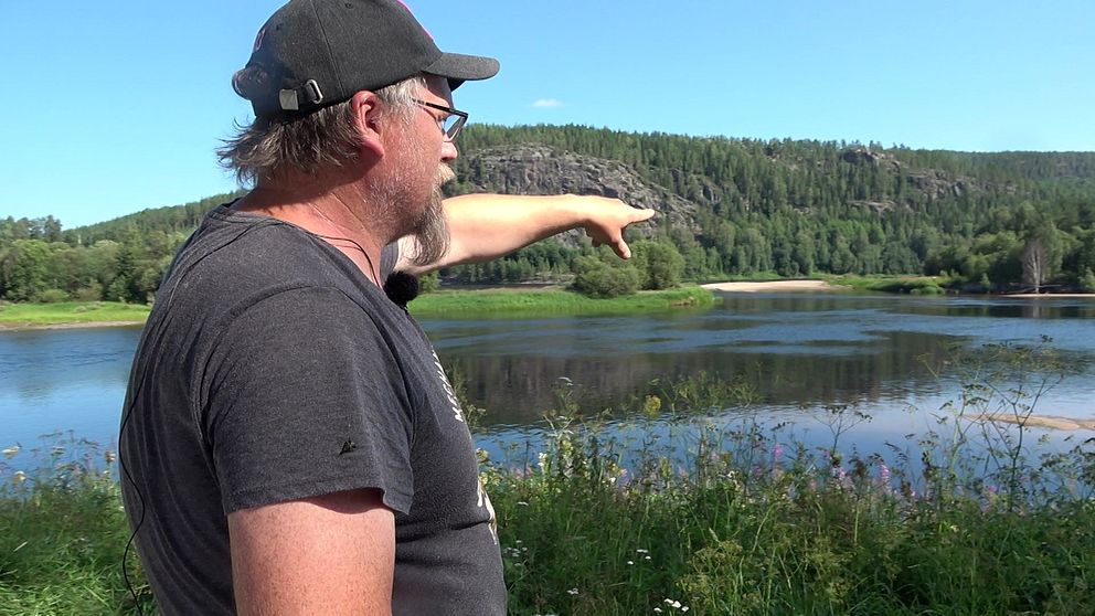 En man med keps står och pekar mot vattnet.