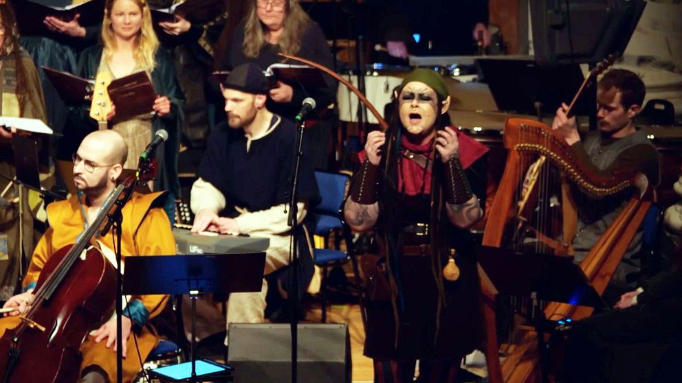 Flera musiker och en sångare uppträder tillsammans på en scen med olika instrument.