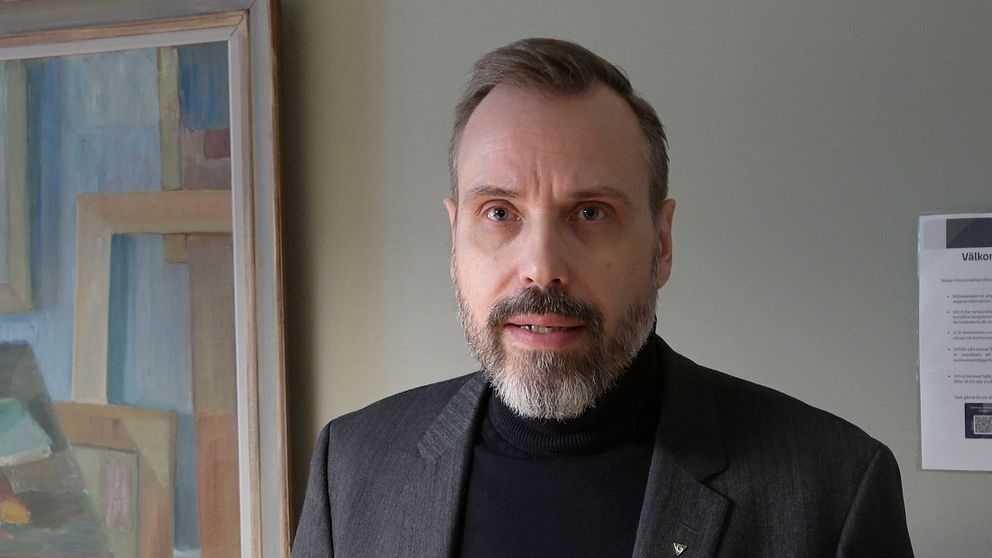 Regiondirektör Håkan Sandahl,  iklädd kavaj, framför en målning och A4-papper uppsatt på vägg.