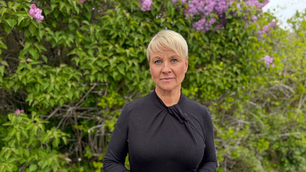 Äldre- och socialförsäkringsminister Anna Tenje (M) står framför blommande buskar utomhus.