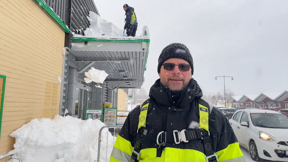 En klättrande skottare står framför en man som skottar taket på en butik.