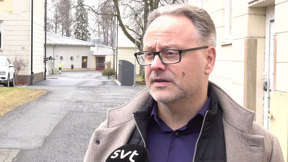 Intervju utomhus, SVT-mikrofon, byggnader i bakgrunden.