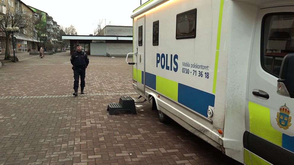 Polisfordon parkerat på öde torg, en person går bortåt i bakgrunden.