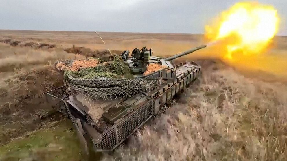 Stridsvagn som avfyrar kanon på ett öppet fält.