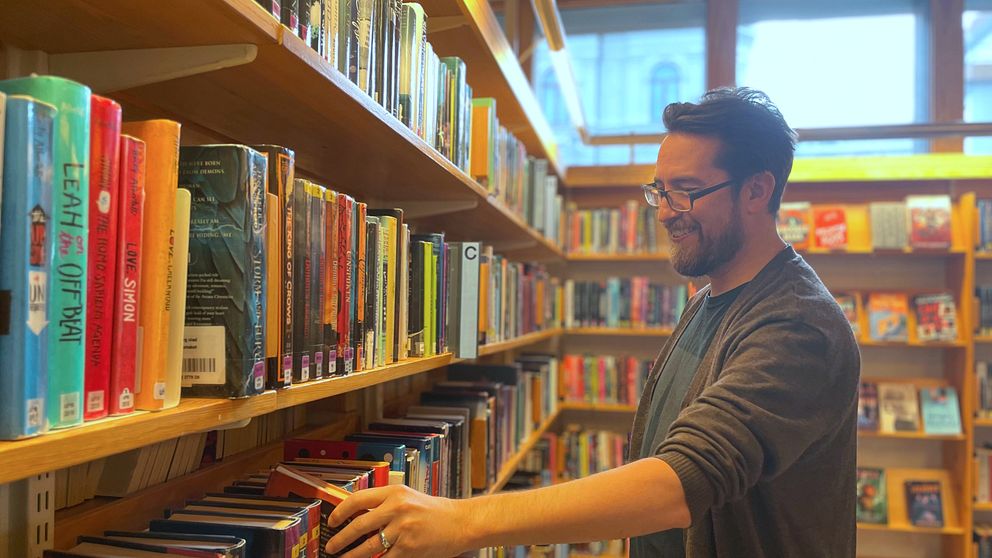 En man vid en bokhylla på ett bibliotek pillar på en bok.