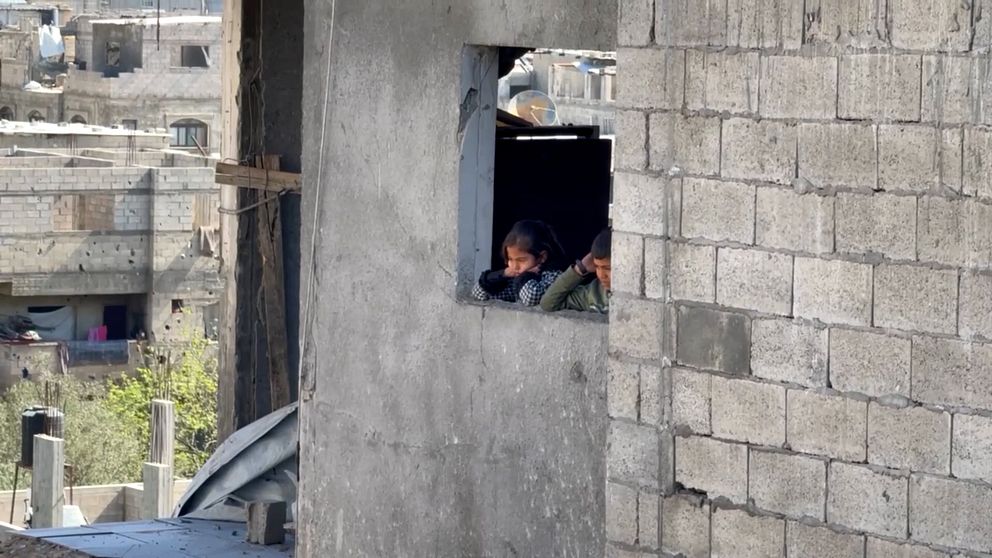 Två barn kikar ut genom ett fönster i en betongbyggnad i Gaza.