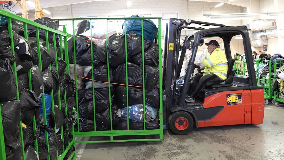 En person kör truck och flyttar bur fylld med svarta sopsäckar på återvinningscentral.