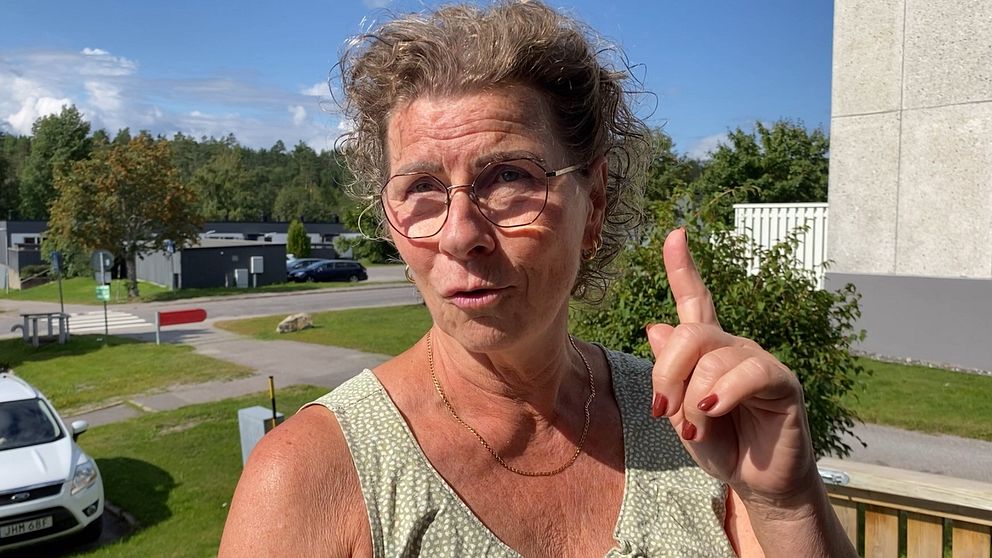Åsa Melander står utanför sin lägenhet och pekar med ett finger upp i luften