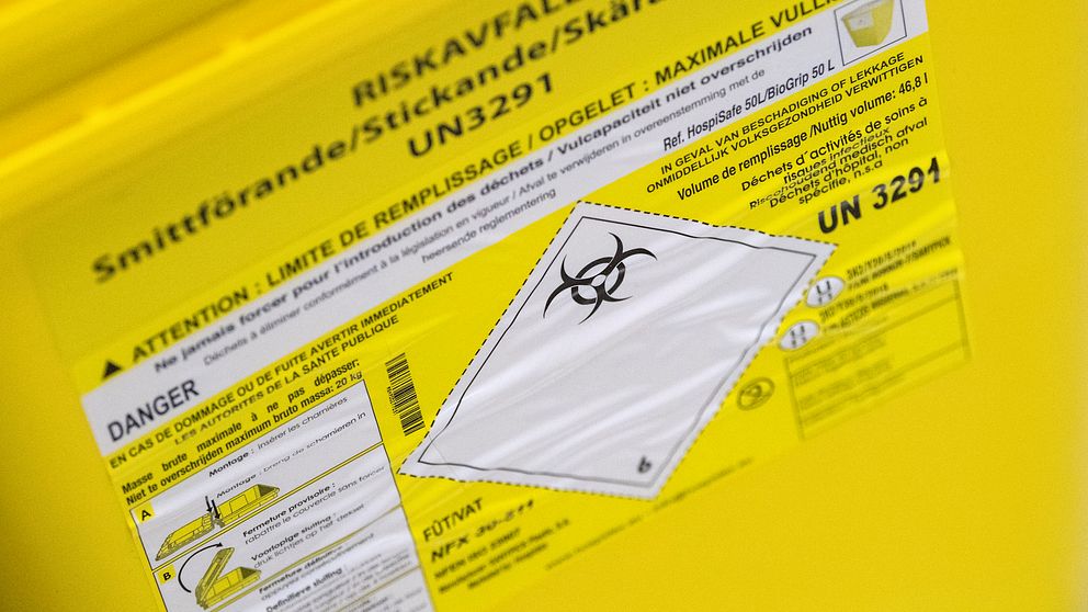 Närbild på gul behållare för smittförande eller stickande avfall med varningssymbol.