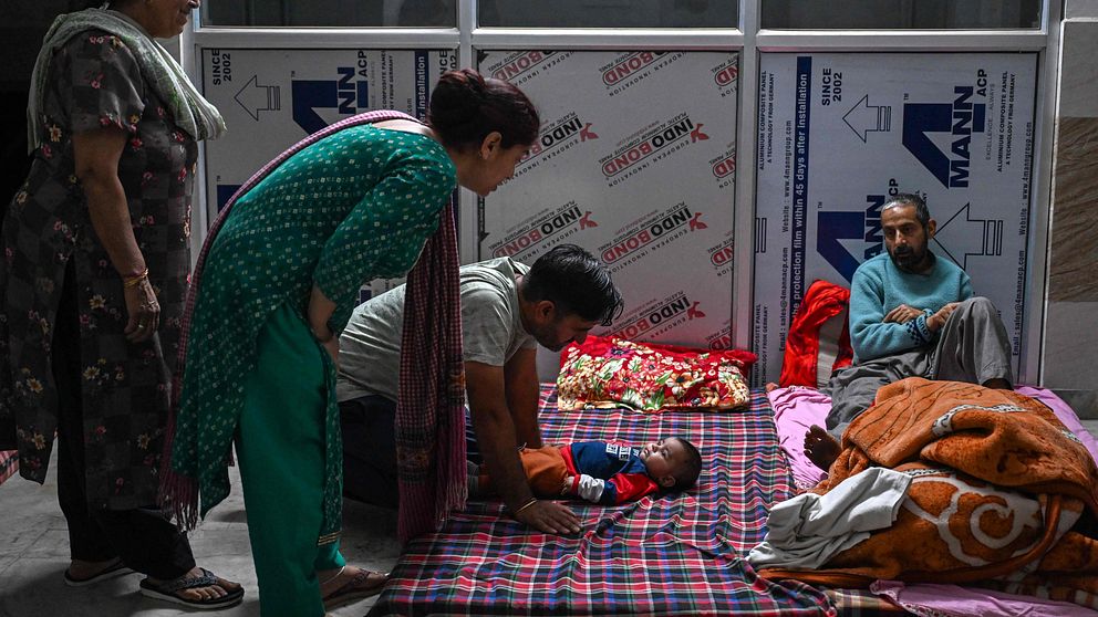 Fyra vuxna och ett barn befinner sig på madrasser på golvet i vad som verkar vara ett tillfälligt skyddsrum i Punch-distriktet i Indien.