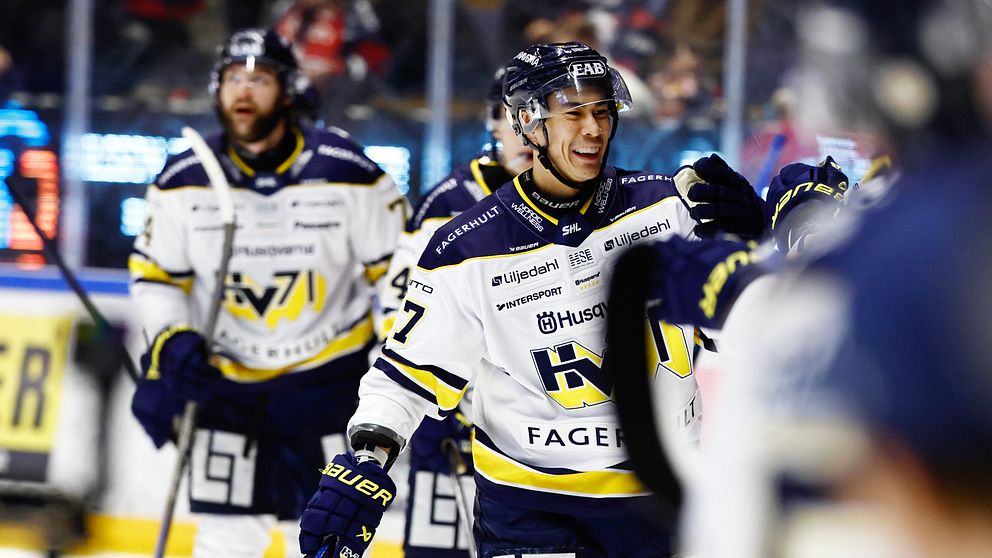 Jonathan Ang firar efter en målskytt, iförda laguniformer med blå och vita färger. Spelarna är i en inomhusarena med andra åskådare i bakgrunden.