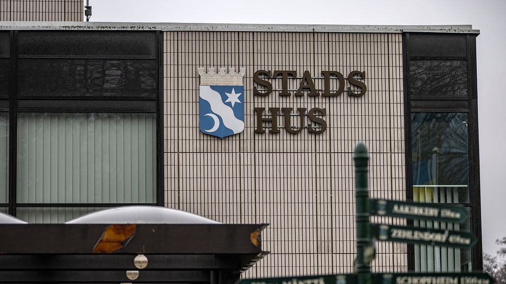 Stads Hus-skylt på en byggnad med en vägskylt i förgrunden som visar riktningar.