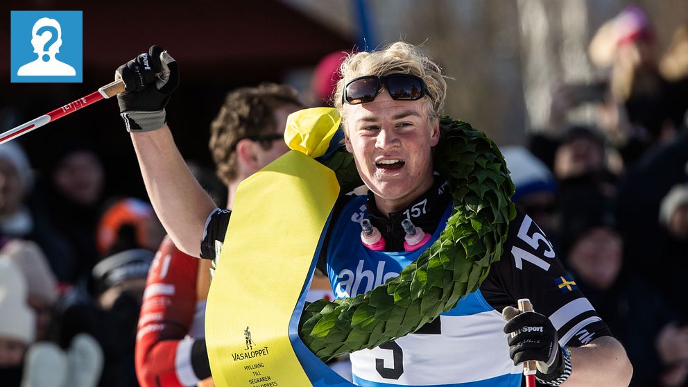Skidåkare firar med krans och banderoll efter lopp, publik i bakgrunden.