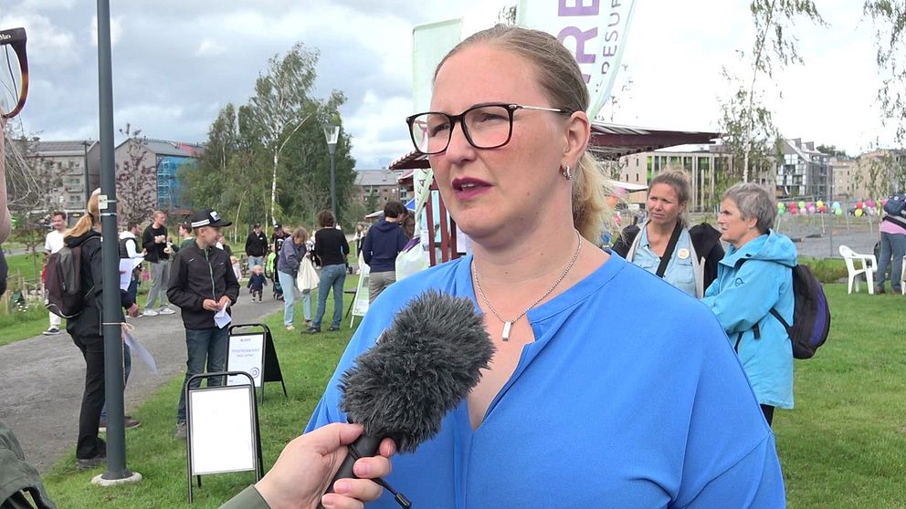 En porträttbild på kommunalrådet Carina Sammeli (S) i blå tröja och svarta glasögon. Många människor i bakgrunden.