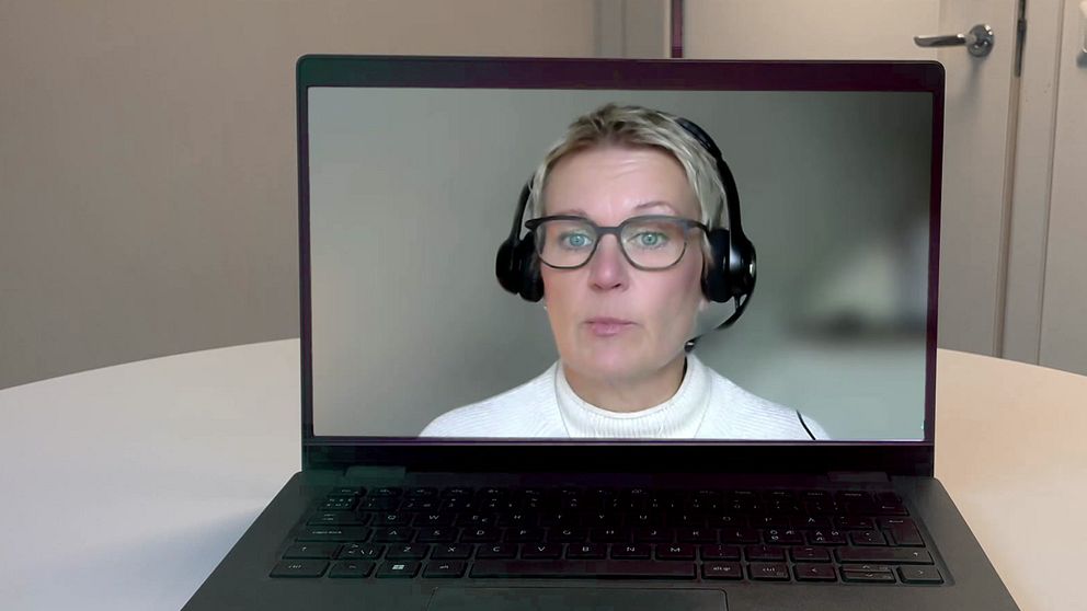 En laptop står på ett bord och visar ett videosamtal. Skärmen visar en person som bär hörlurar och en vit tröja, medan bakgrunden är oskarp.