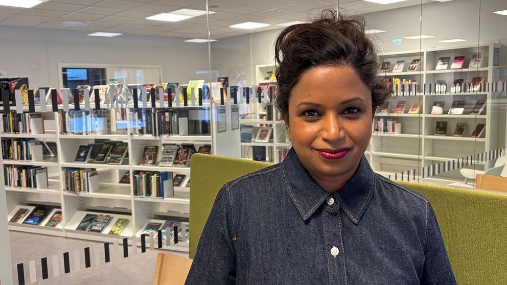 En person står i en modern biblioteksinteriör omgiven av hyllor fyllda med böcker.