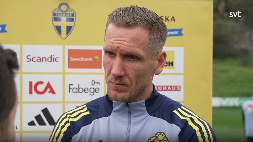 Person i Sveriges fotbollslandslags träningsoverall vid en presskonferens.