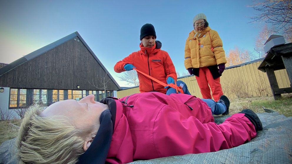 Personer övar första hjälpen utomhus, en person ligger ned medan två står och instruerar.