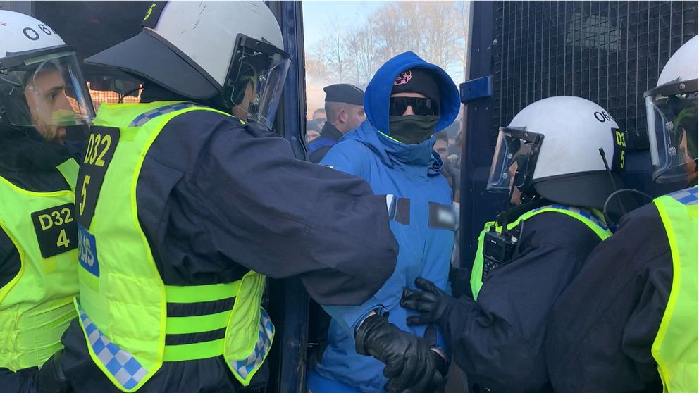 Bild på poliser som tar tag i en maskerad man med solglasögon och huva.