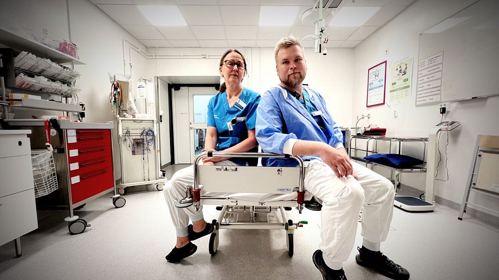 Två sjukvårdsanställda sitter på en brits i ett sjukhusrum.