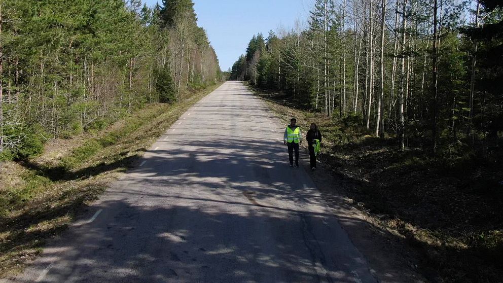 Två personer med reflexväst går på en väg med en blodfläck på.